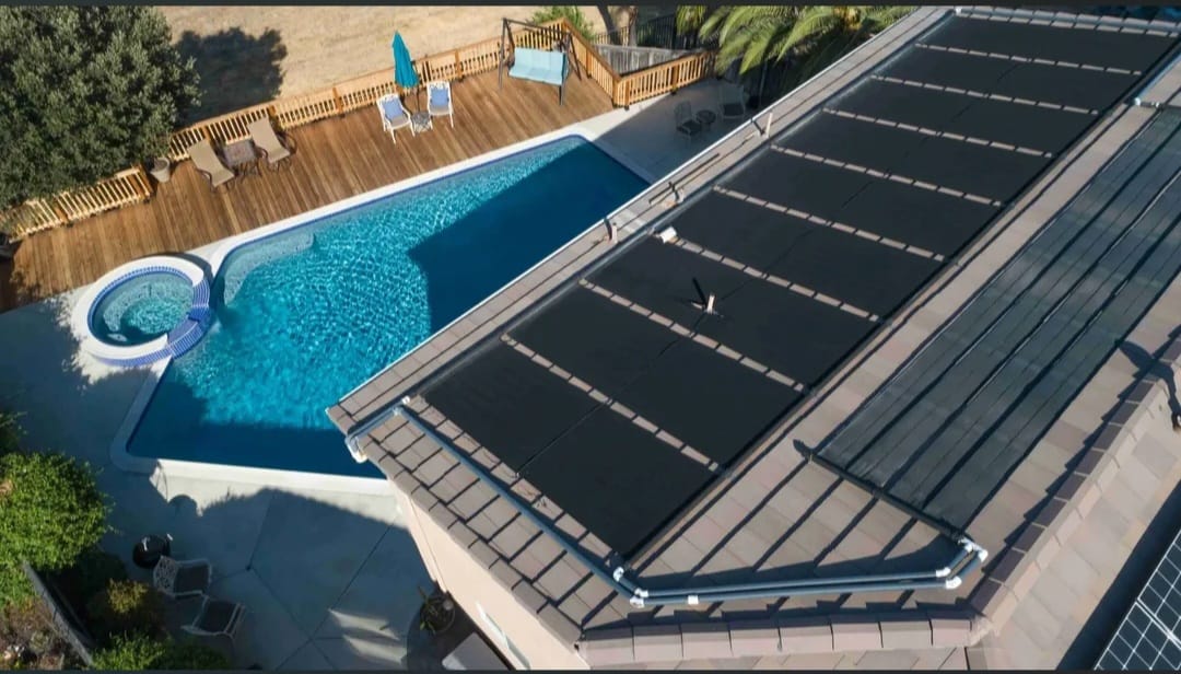 Aerial view of a residential pool with solar pool heating panels installed on the adjacent roof